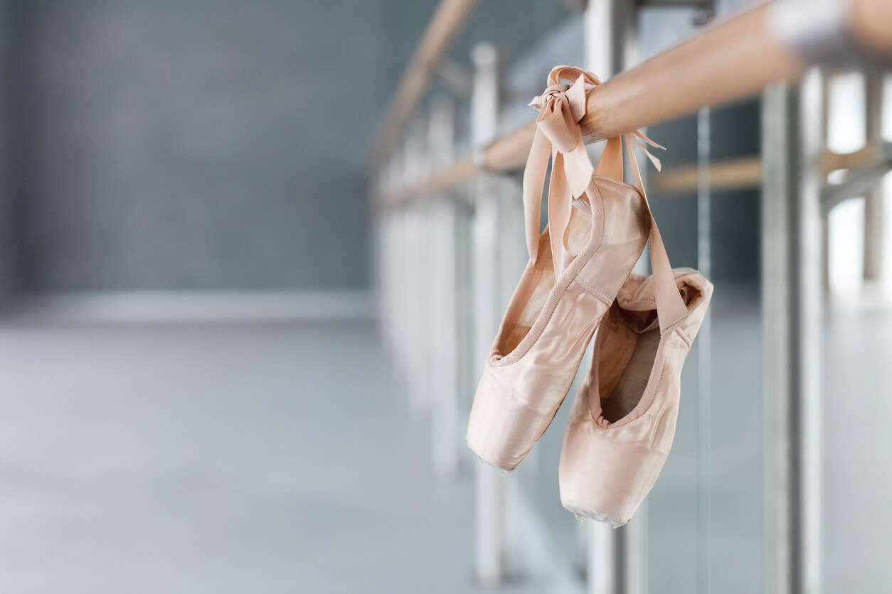 a pair of pink silk ballet slippers tied to a ballet barre in a mirrored dance studio