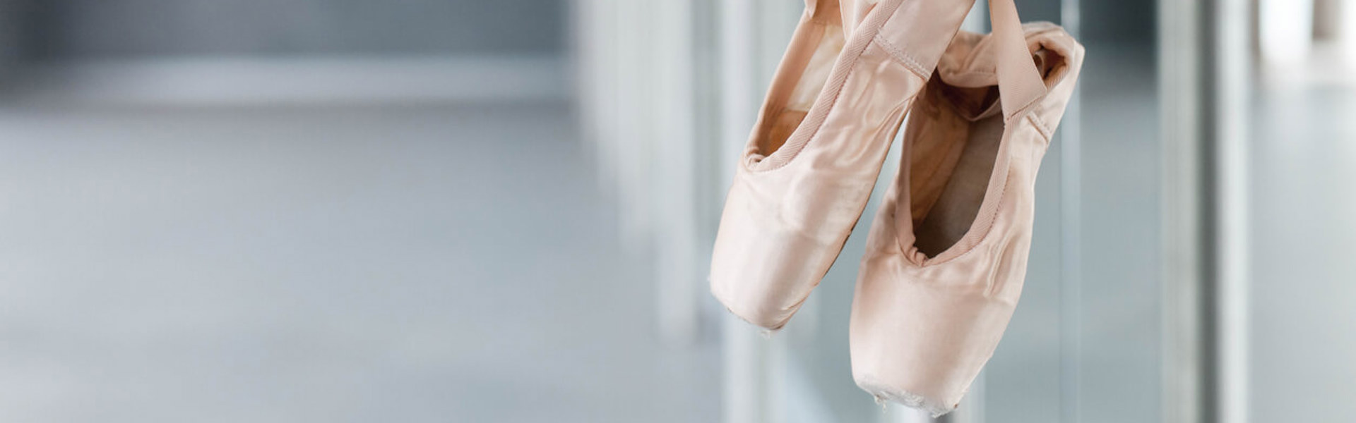 a pair of pink silk ballet slippers tied to a ballet barre in a mirrored dance studio