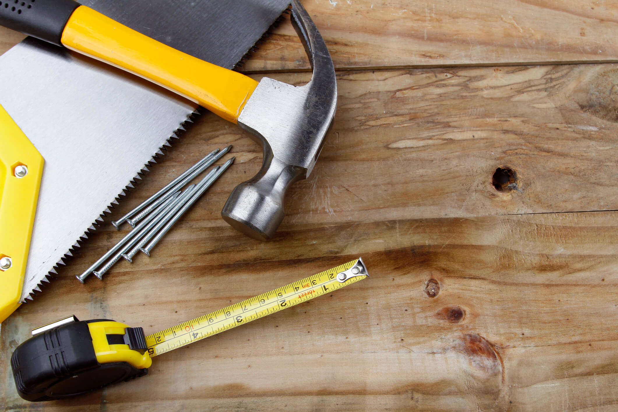 carious DIY tools like a hammer and nails and measuring tape on a wooden background