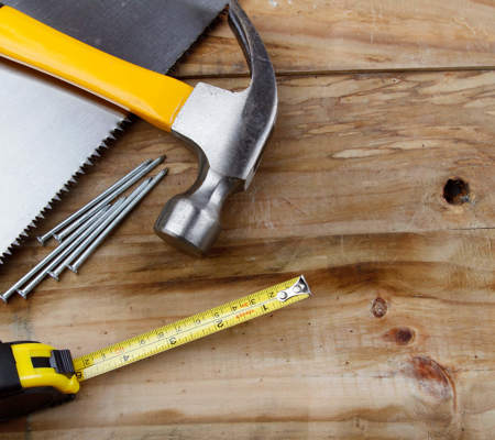 carious DIY tools like a hammer and nails and measuring tape on a wooden background