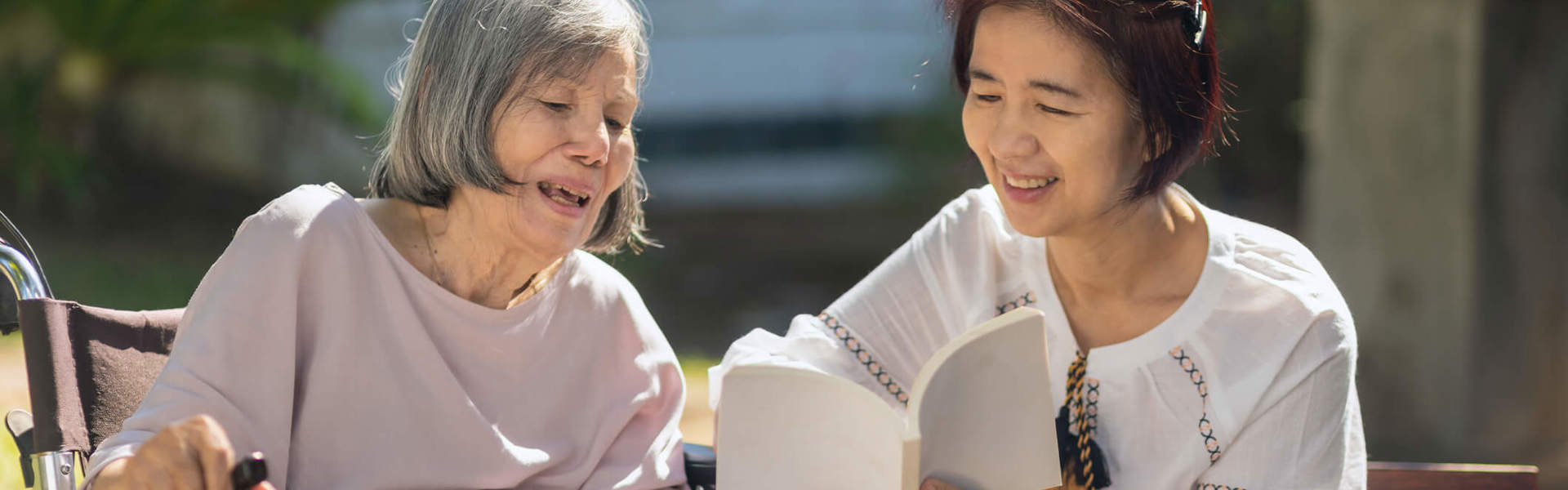 Main Image: an adult daughter reading with her elderly mother with Dementia outside.