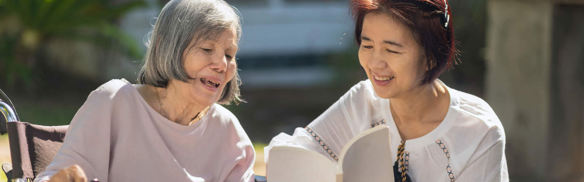 Main Image: an adult daughter reading with her elderly mother with Dementia outside.