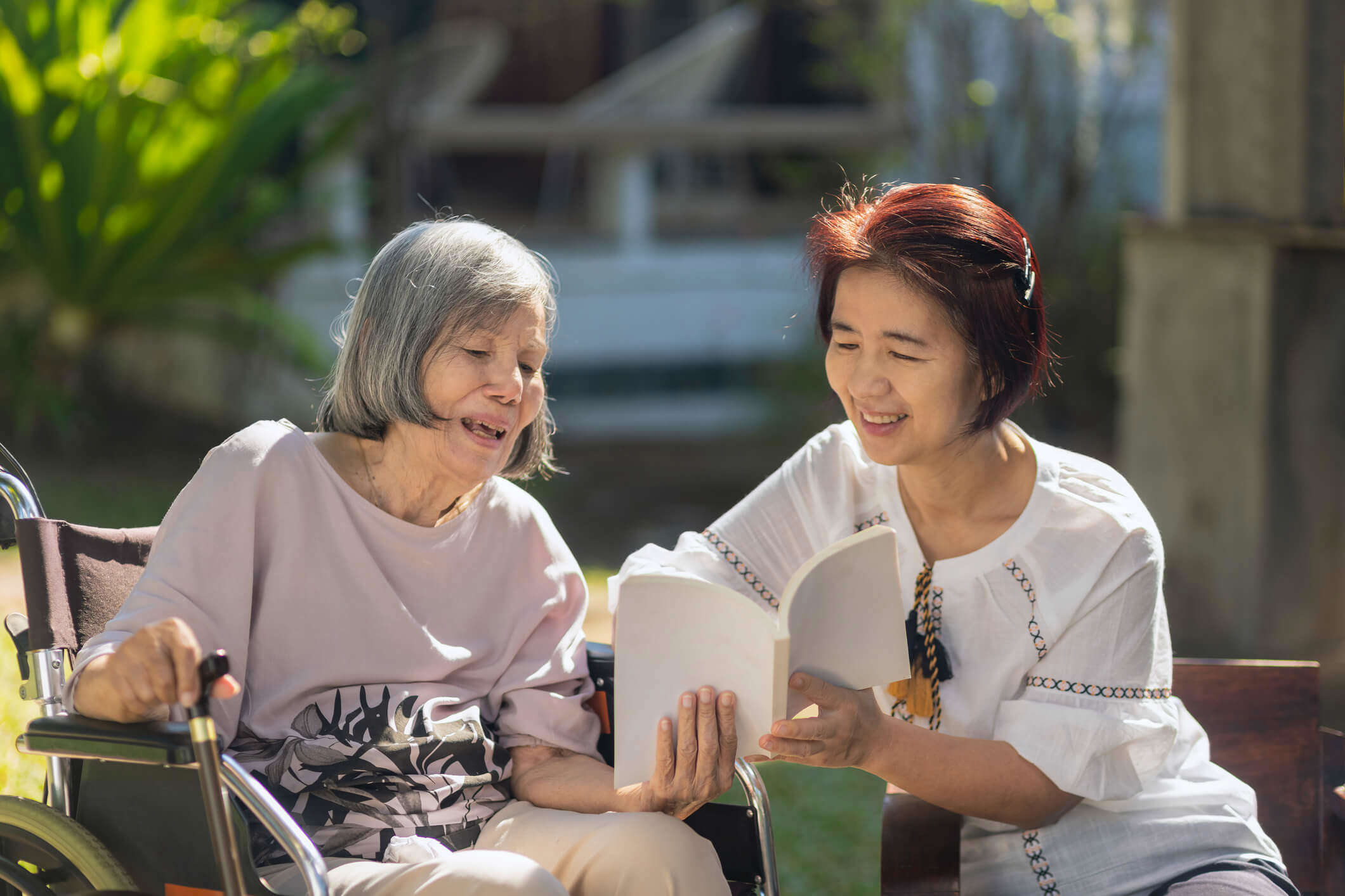 Main Image: an adult daughter reading with her elderly mother with Dementia outside.