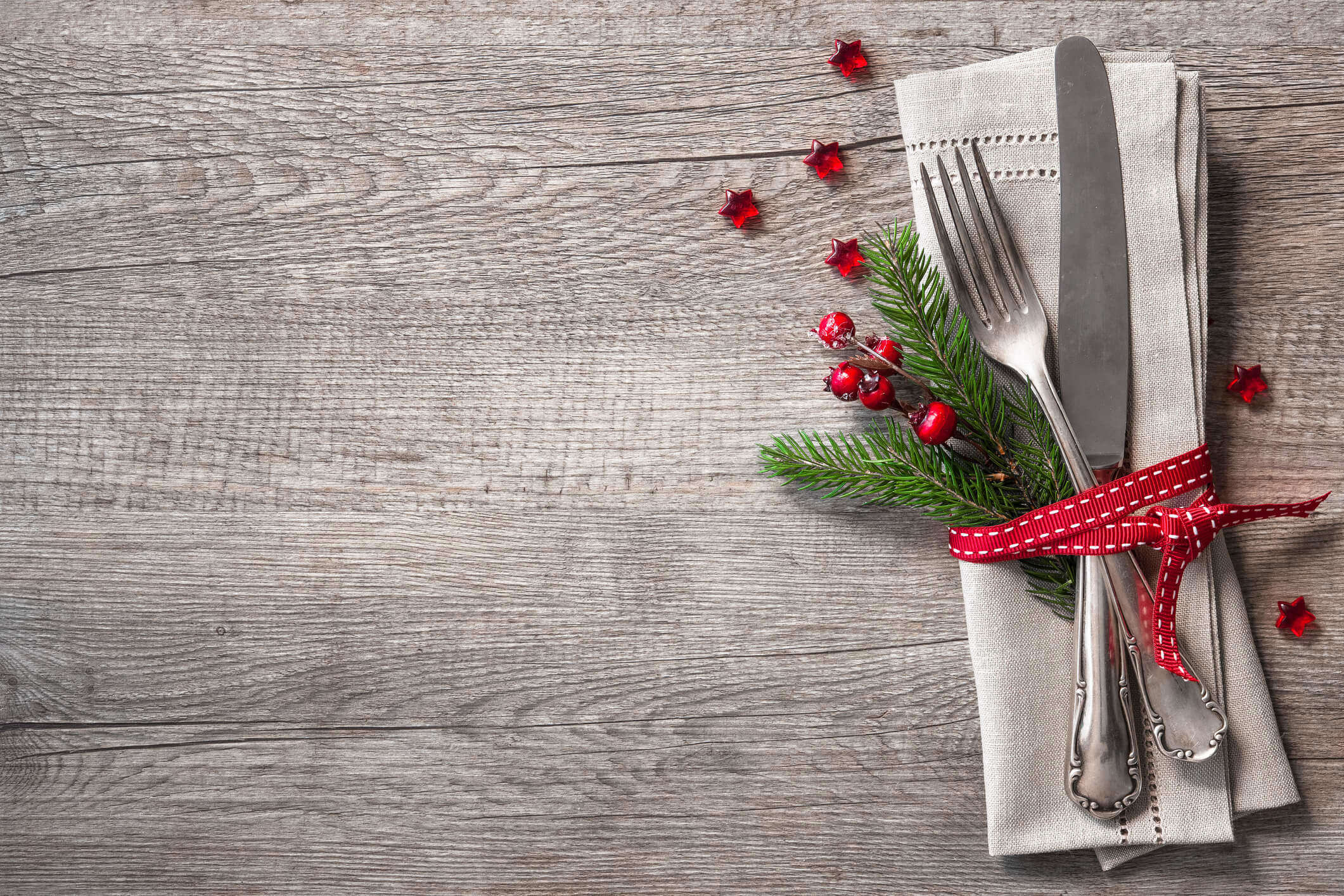 a set of cutlery in a festive napkin holder decorated with Christmas tree fern and red berries