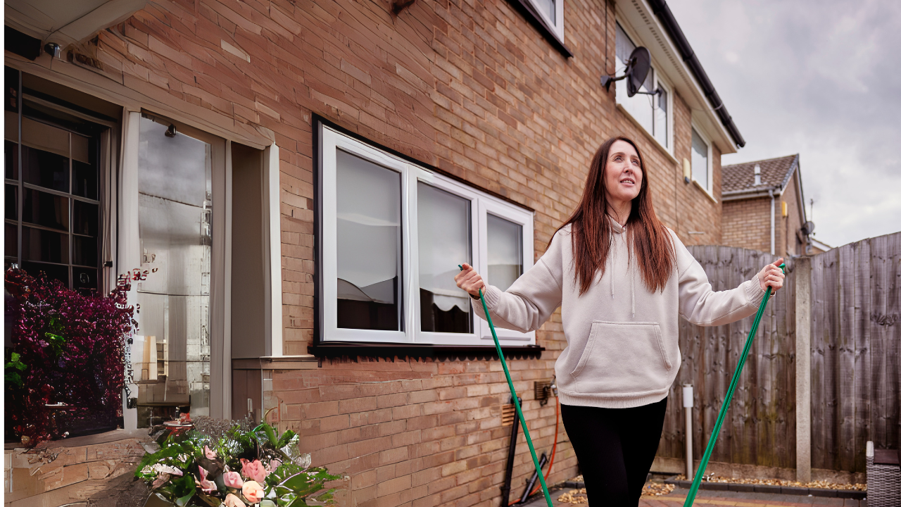 Main image: a woman in her garden using a resistance band to stretch before a Mobilates class.