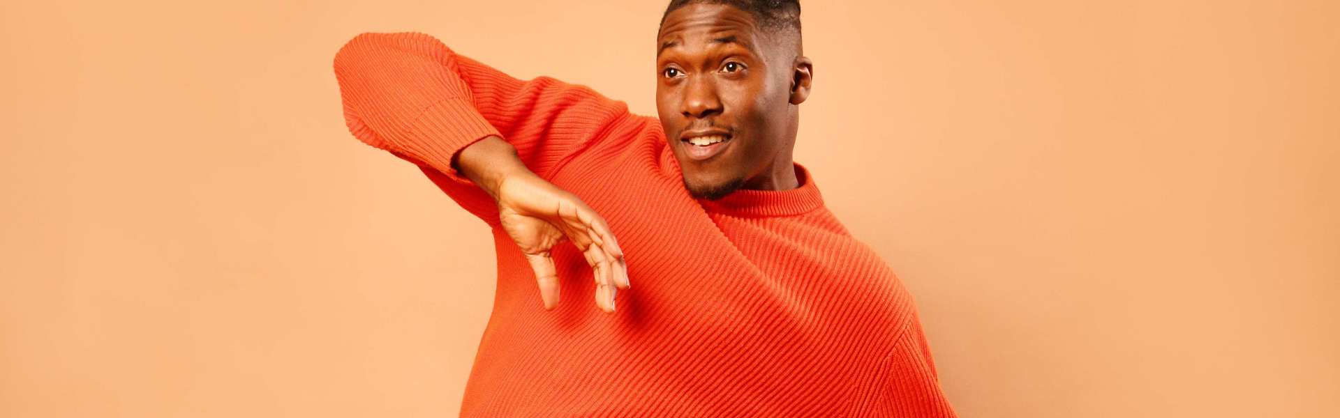 Photo of Daniel Browne AKA Mr Groove dancing in an orange jumper, infront of an orange background.