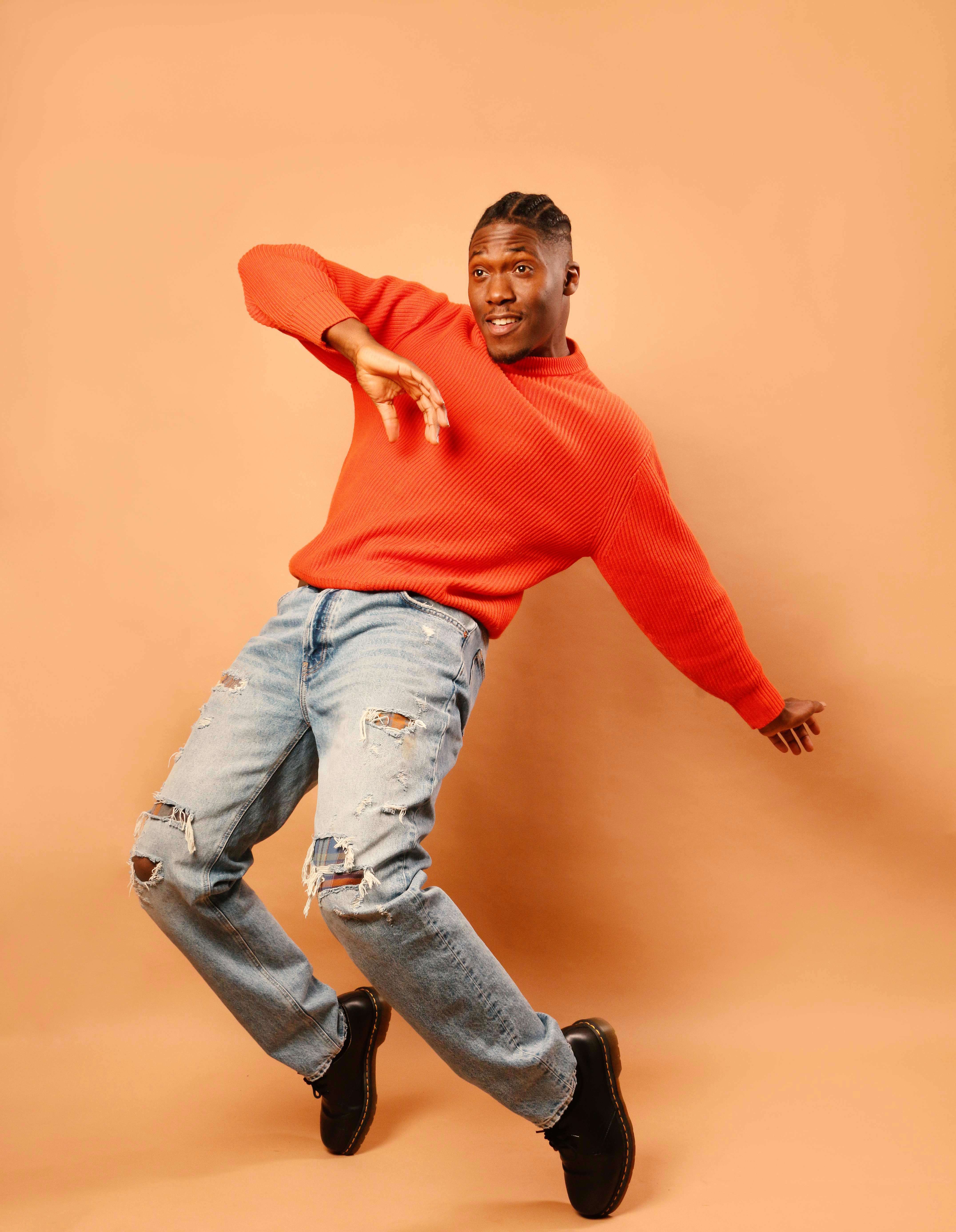 Photo of Daniel Browne AKA Mr Groove dancing in an orange jumper, infront of an orange background.